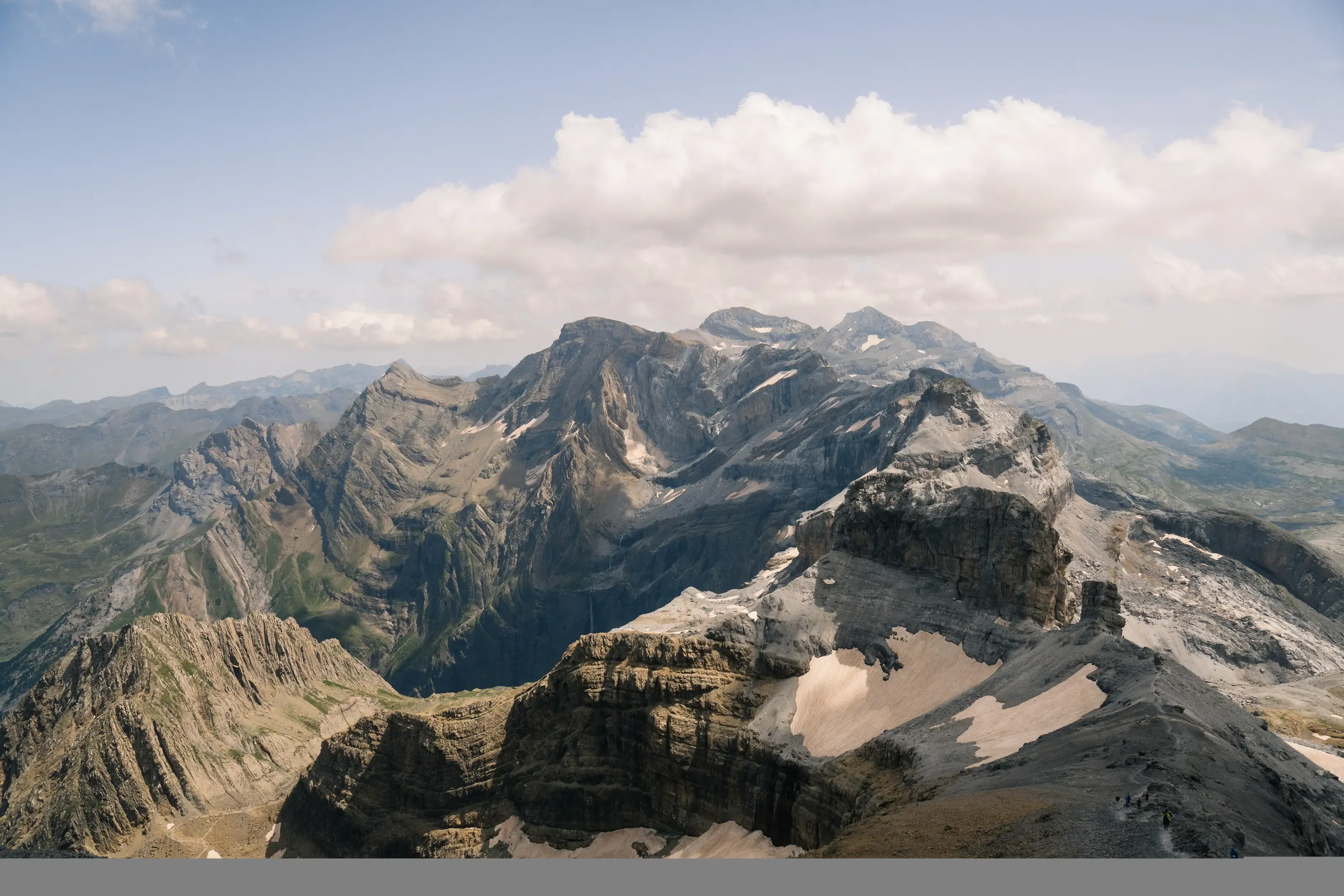 Une vue panoramique de hauts sommets rocheux et escarpés parsemés de plaques de neige sous un ciel partiellement nuageux.